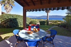 Un espacio al aire libre cubierto con una mesa preparada para dos, rodeada de sillas, con vistas a un paisaje que incluye agua y montañas.