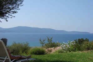 A person seated on a lounge chair overlooking a body of water with distant landforms. - Holiday home with 2 bedrooms (OLMETO PLAGE)