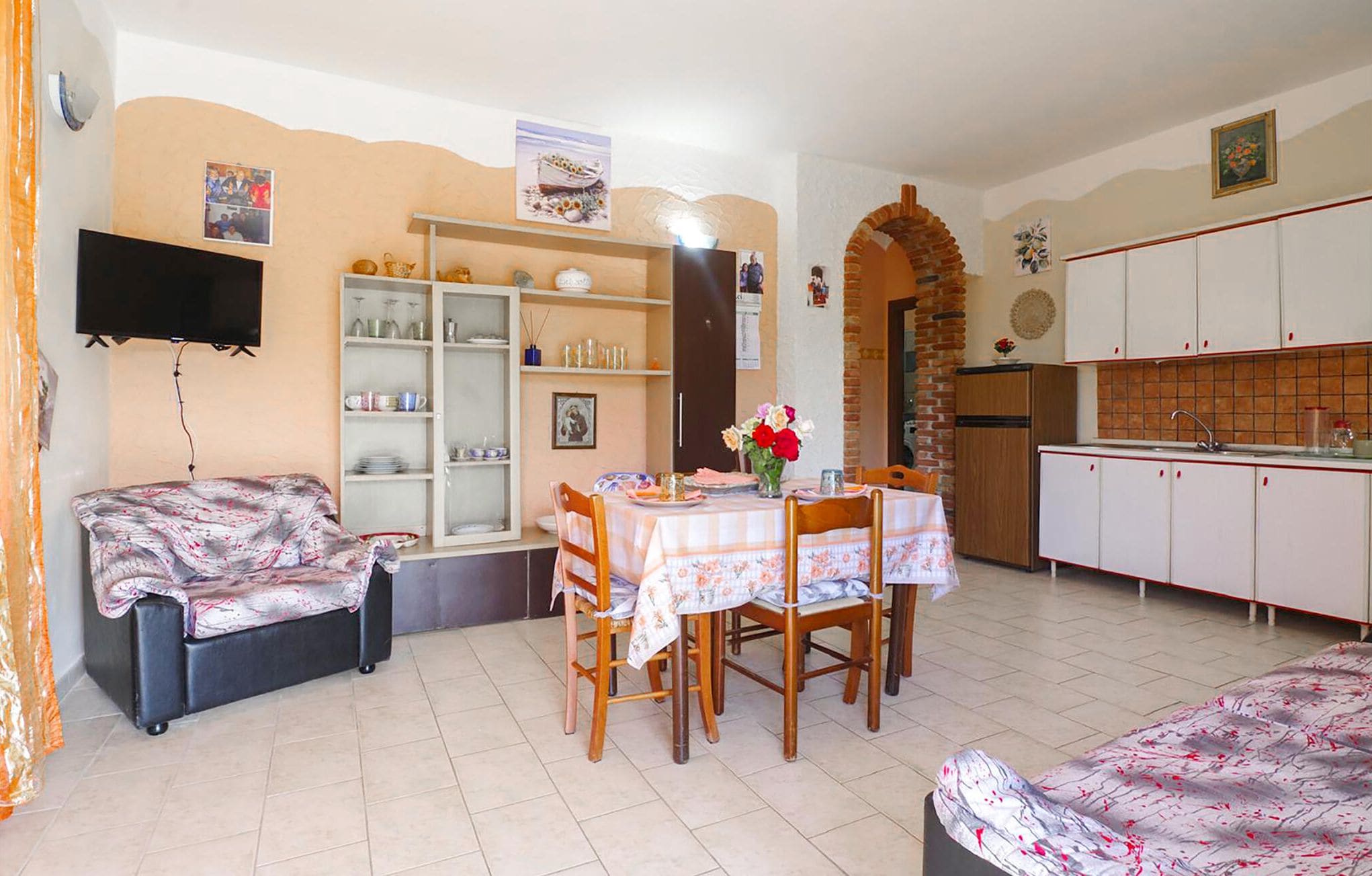 A compact living space with a dining area, kitchenette, and a TV mounted on the wall.