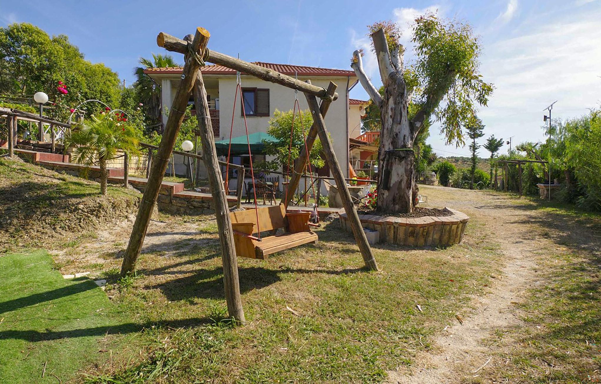 Un ensemble de balançoires en bois installé sur une pelouse, avec une maison en arrière-plan.