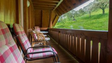 A covered porch with wooden railings, a row of checkered chairs, and a view of a green landscape with trees.