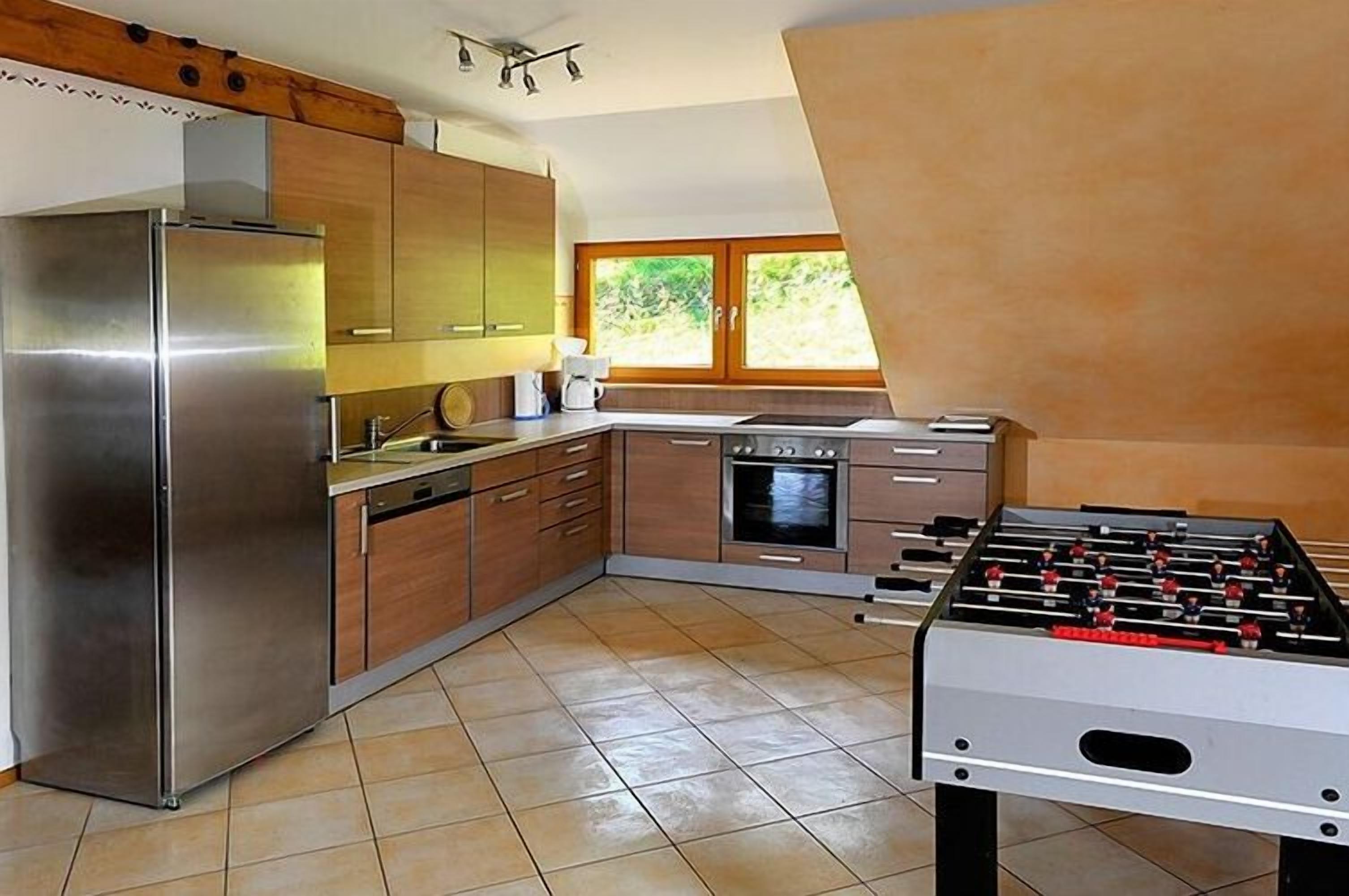 A modern kitchen with a foosball table, stainless steel appliances, and wooden cabinets.