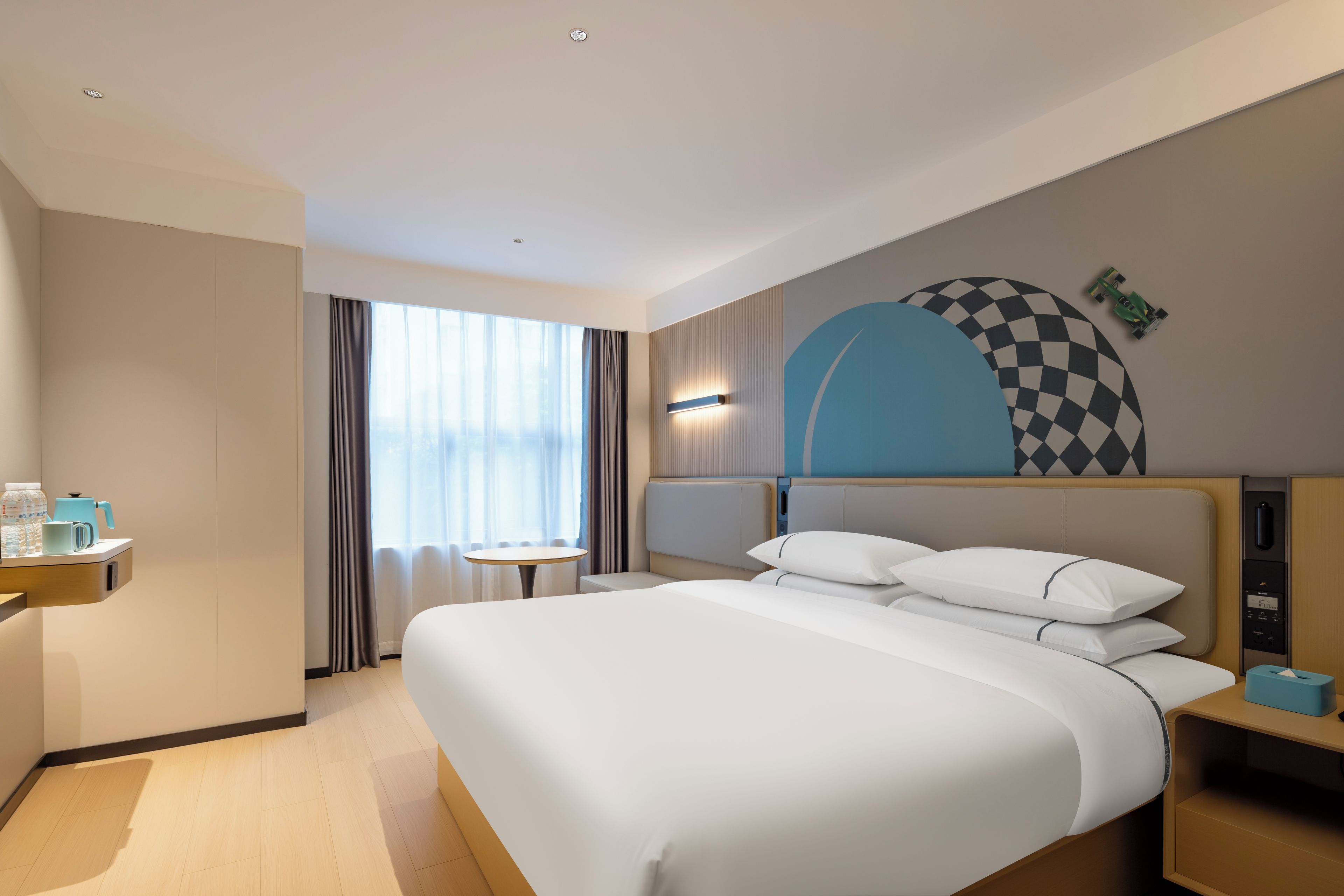 A hotel room with a large bed, bedside tables, a small table, and a window with curtains.