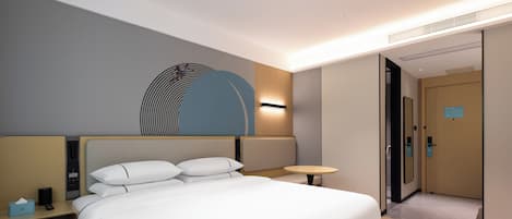 Une chambre d’hôtel moderne avec un grand lit, des tables de chevet, une lampe fixée au mur et une porte donnant sur une autre pièce.