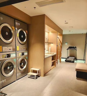 A laundry room with multiple washing machines, a small table, and a treadmill. - City Comfort Inn (Guangzhou)