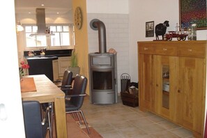A kitchen with a wood-burning stove, a dining table with chairs, and a cabinet with glass doors. - Holiday home in Husum with swimming pool (Husum)