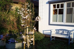 A white brick building with a white bench and a wooden trellis with flowering plants. - Holiday home in Husum with swimming pool (Husum)