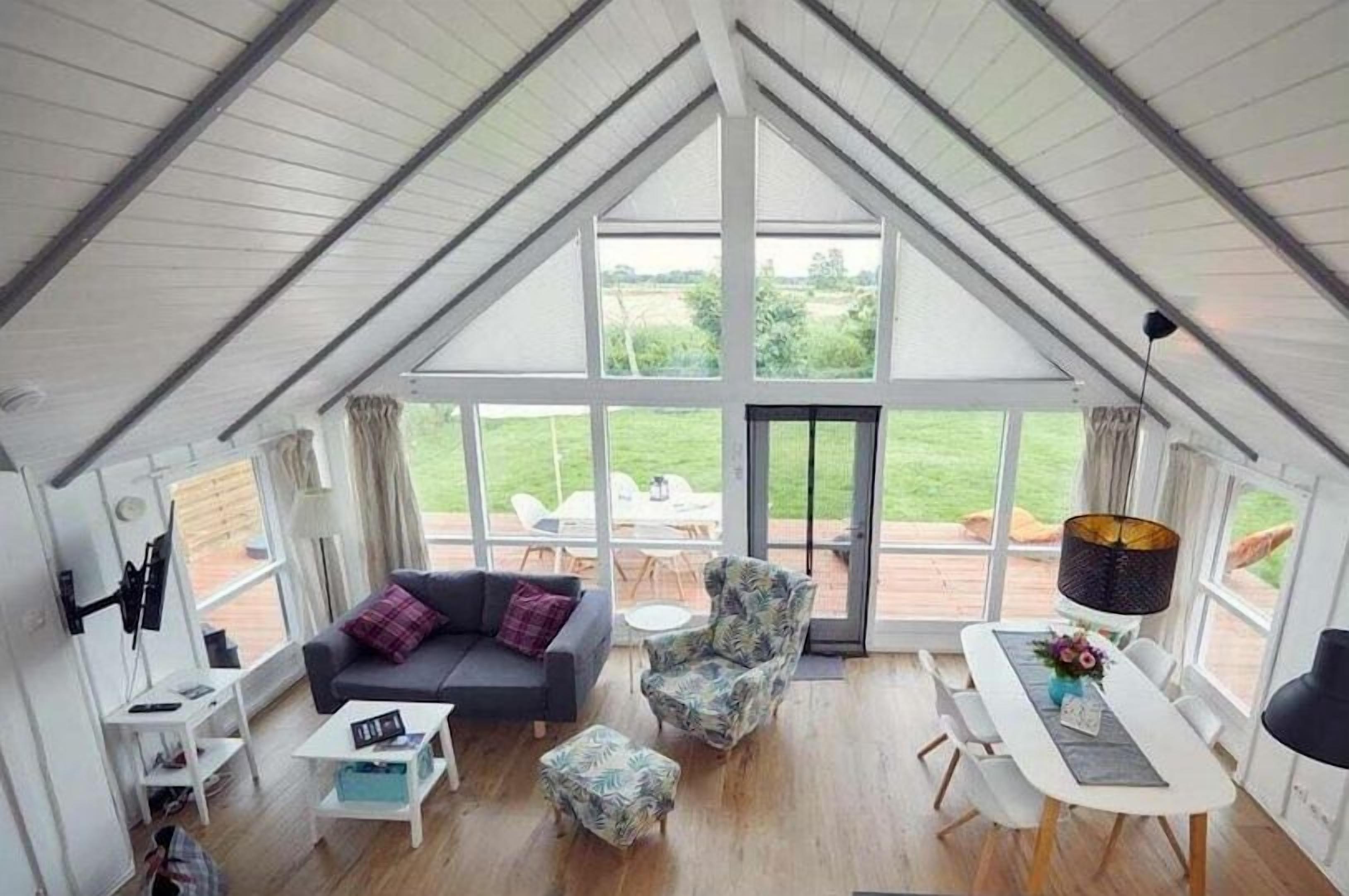A spacious room with a high ceiling, a sofa set, a dining table, and a view through large windows.