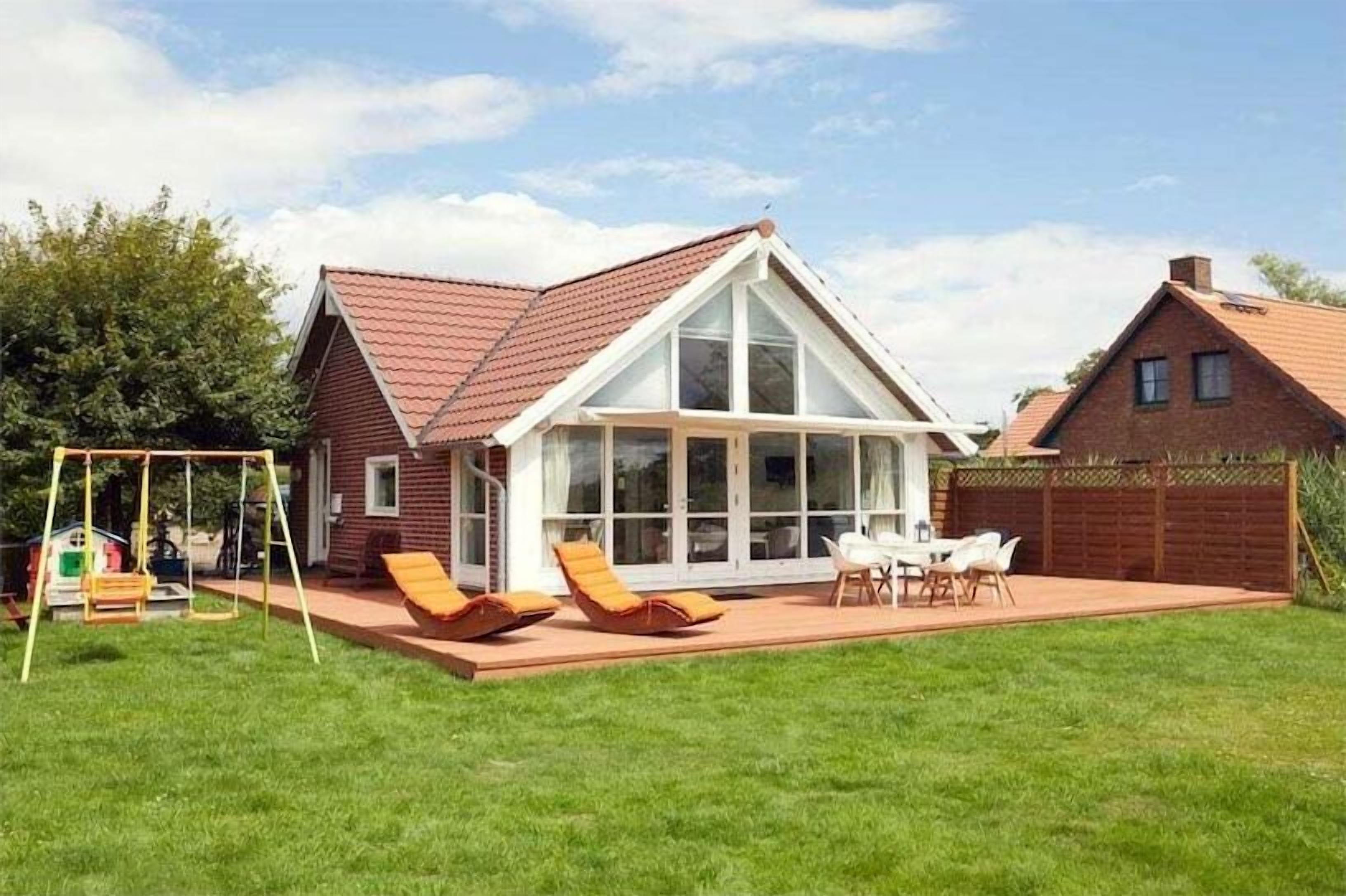 Une maison avec une grande façade vitrée, un patio avec des chaises et un portique avec des balançoires.