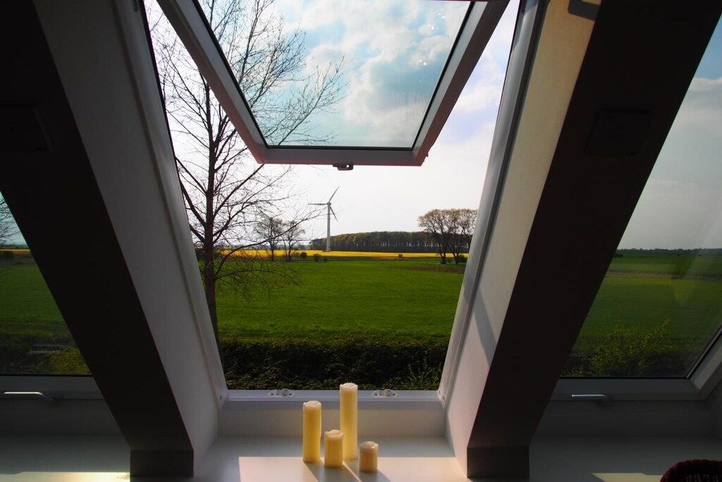 A skylight window with a view of a green field and a wind turbine.