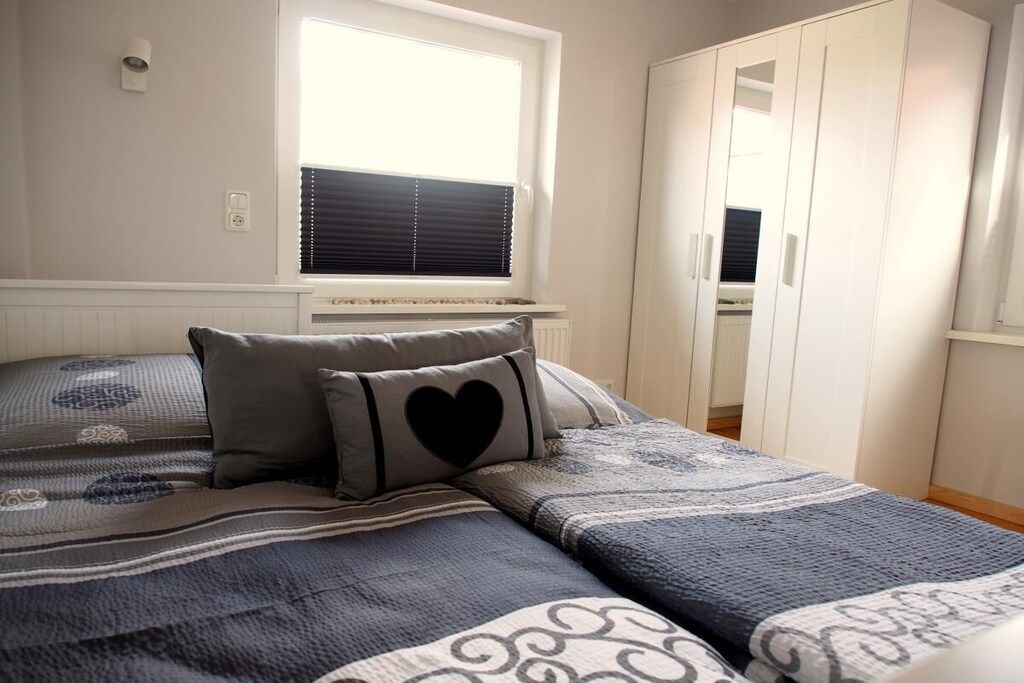 A bedroom with a bed, a window with blinds, a wardrobe, and a radiator.