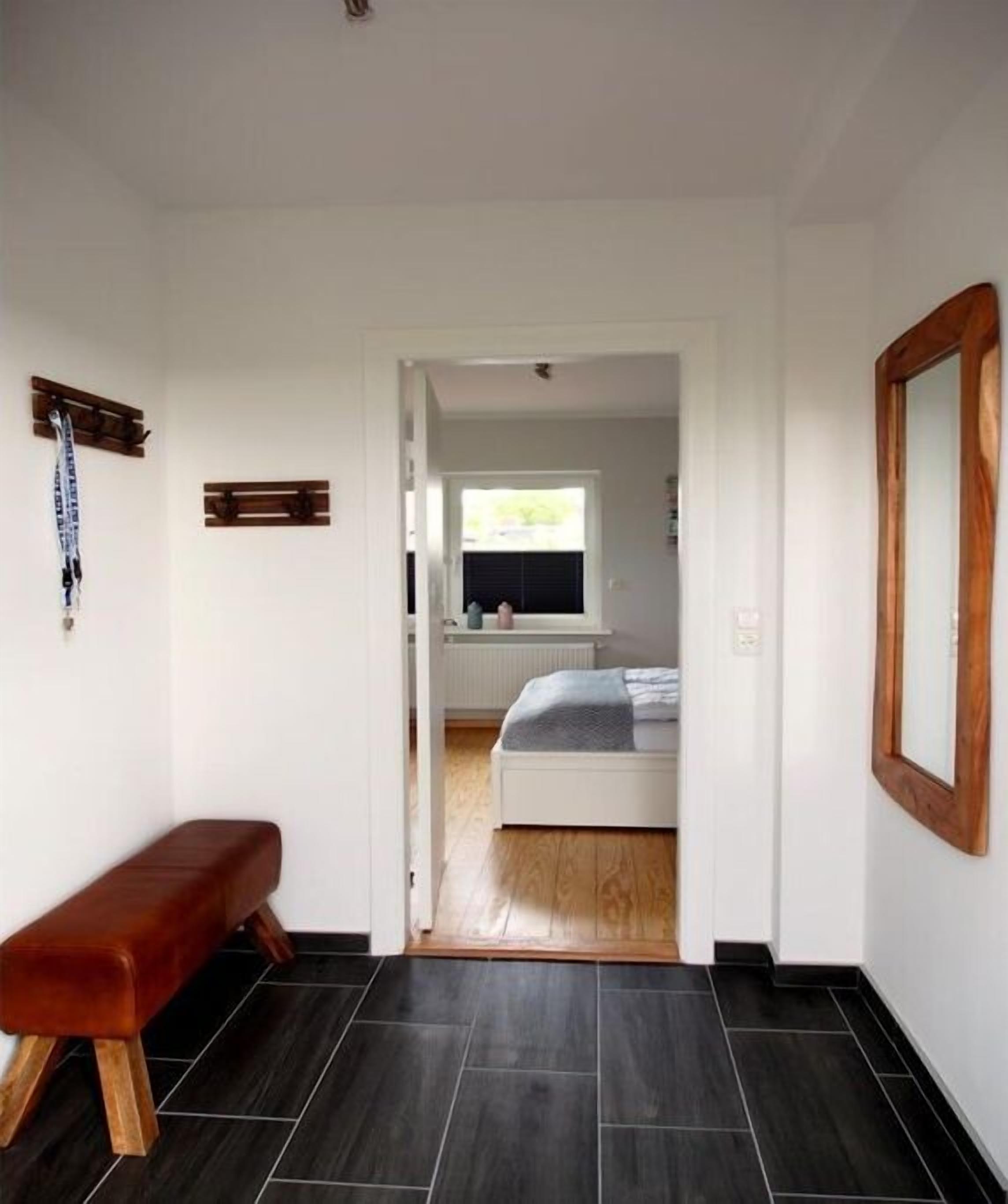 Un pasillo que conduce a un dormitorio con una cama, un banco y un espejo en la pared.