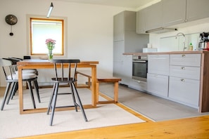 A modern kitchen with grey cabinets, a wooden dining table, and a built-in oven. - Holiday home with 1 bedroom (Kalifornien)