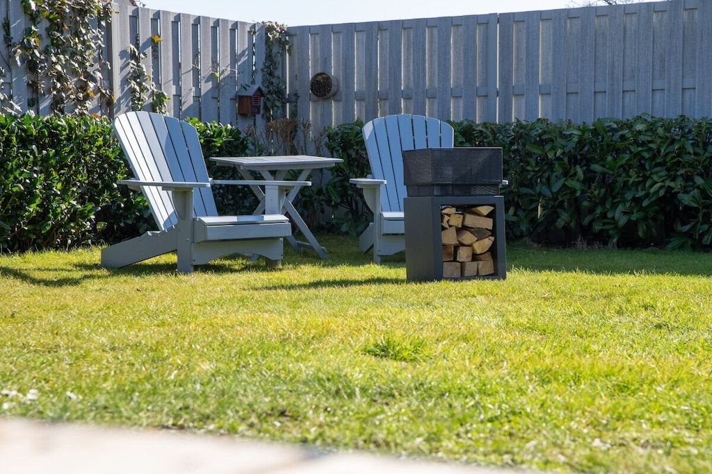 A backyard with two Adirondack chairs, a small table, and a woodpile.
