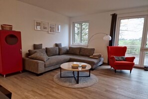 Ein modernes Wohnzimmer mit einer Eckcouch, einem roten Sessel, einem Couchtisch und einem großen Fenster mit Blick.