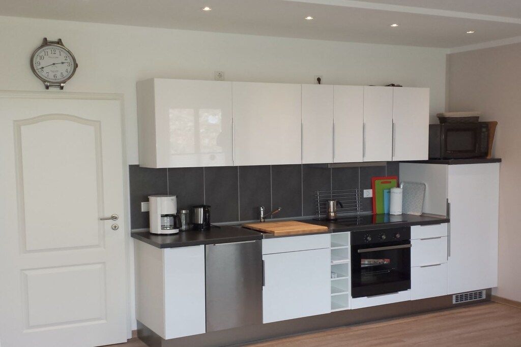 A modern kitchen with white cabinets, a microwave, a coffee maker, and a clock on the wall.