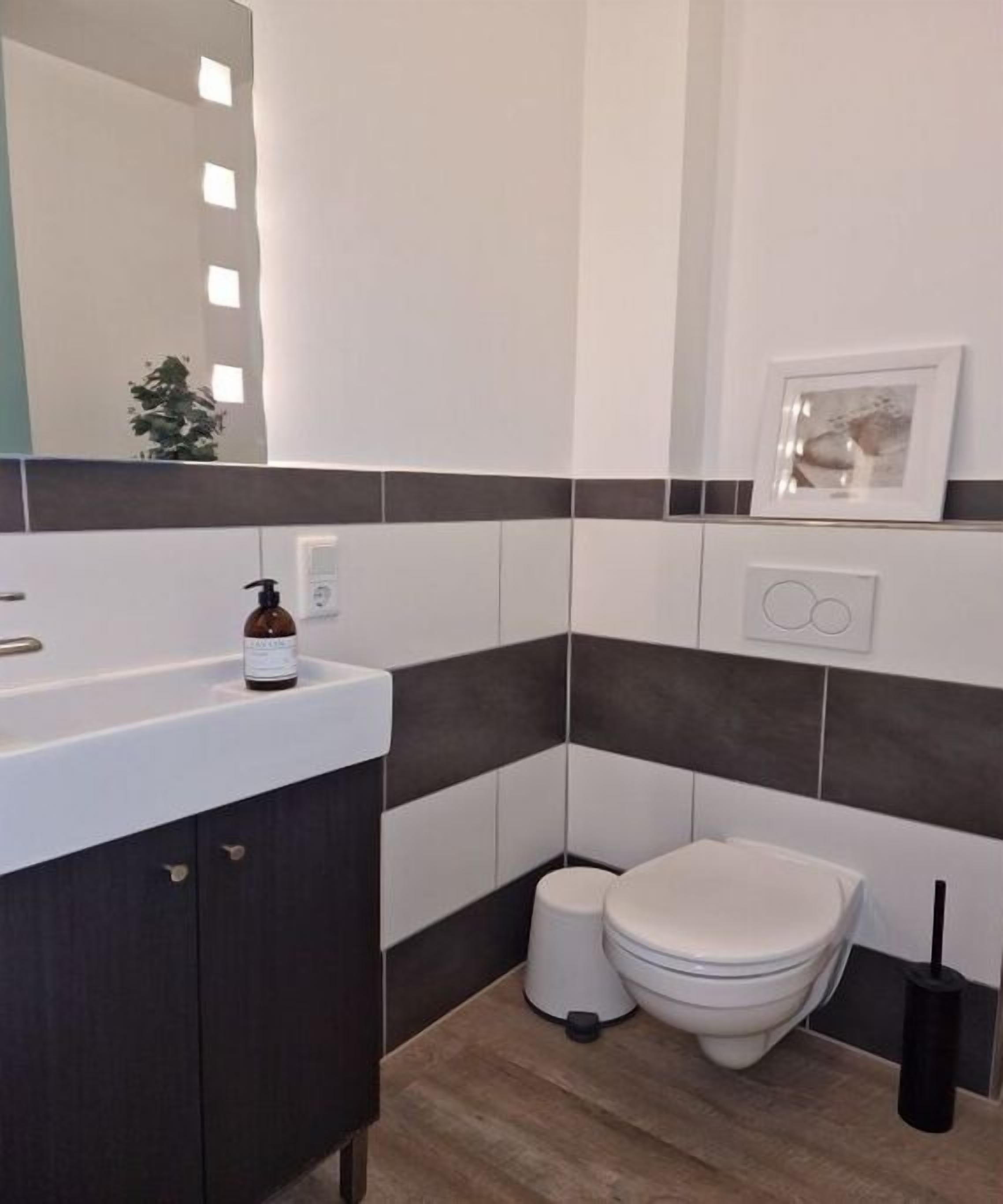 A modern bathroom with a white sink, dark-toned tiles, a toilet, and a framed picture on the wall.