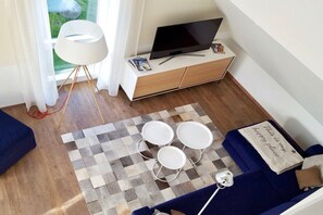 A modern living room with a TV, sofa, and a small table with a checkered rug. - Holiday apartment with 1 bedroom (Krummhörn \/ OT Greetsiel)