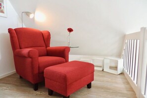Una poltrona vermella amb otomana en una habitació amb un radiador blanc, una taula petita amb un vas i una imatge a la paret.