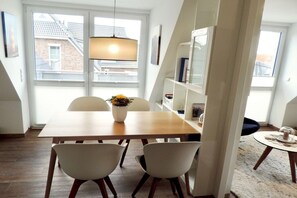 A dining area with a wooden table, white chairs, a vase with flowers, and a pendant light. - Holiday apartment with 1 bedroom (Krummhörn \/ OT Greetsiel)
