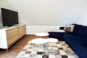 Un saló modern amb televisió plana, un sofà blau fosc i una taula de cafè blanca.