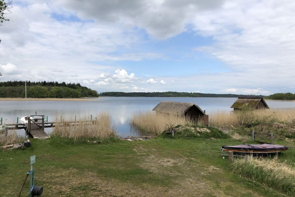 A lakeside property with a dock, two thatched-roof cabins, and a grassy area.