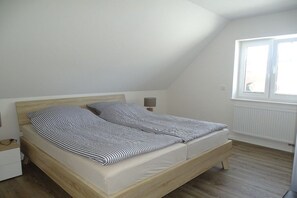 A single bed in a room with a sloped ceiling, a bedside table, a lamp, and a window. - Holiday apartment with 1 bedroom (Seedorf)