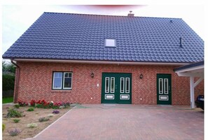 A brick house with a tiled roof, two green doors, and a small window. - Holiday apartment with 1 bedroom (Seedorf)