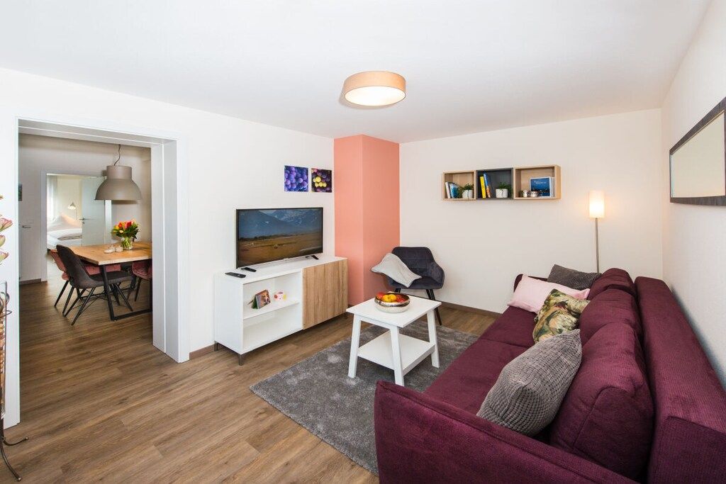 Uma sala de estar moderna com sofá, televisão, área de jantar e corredor que leva a outro quarto.