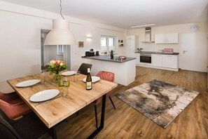 Eine moderne Küche mit weißen Schränken, einer zentralen Kochinsel und einem Essbereich mit einem Holztisch für zwei Personen.