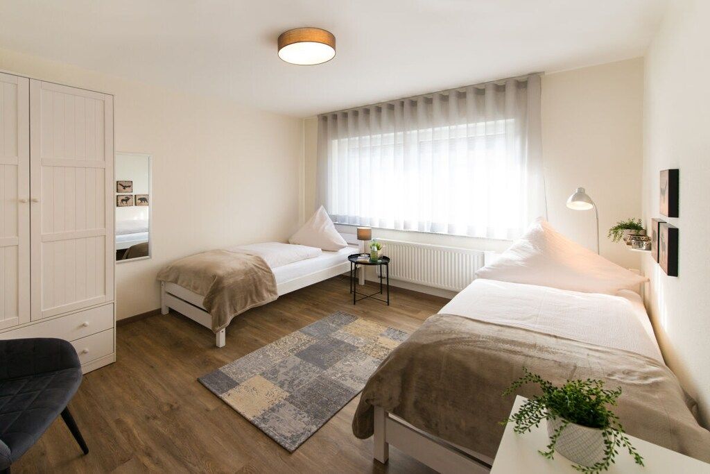 A bedroom with two beds, a wardrobe, a desk with a lamp, and a window with curtains.