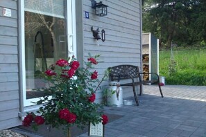Ein Haus mit Veranda, einer Bank, einer Blütenhecke und einem Laternen an der Wand.