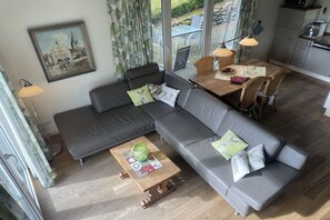 Ein modernes Wohnzimmer mit einem grauen Ecksofa, einem Holztisch und einem Essbereich mit Tisch und Stühlen.