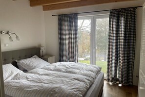 Ein Schlafzimmer mit einem Bett, einem Nachttisch, einer Lampe und einem Fenster mit Vorhängen.