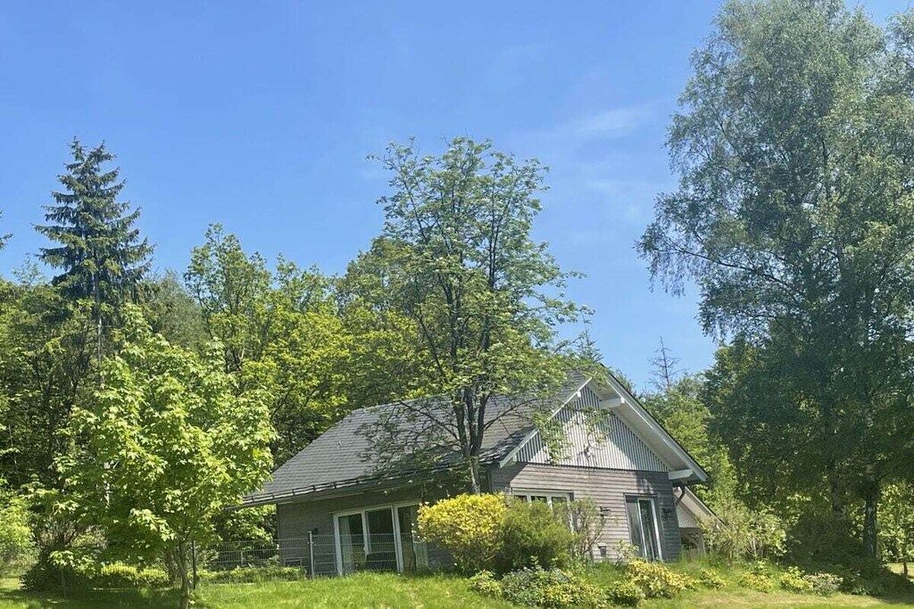A single-story house with a gabled roof, surrounded by trees and greenery.