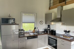 Eine moderne Küche mit Edelstahlgeräten, einem Fenster mit Jalousien und Blick ins Freie.