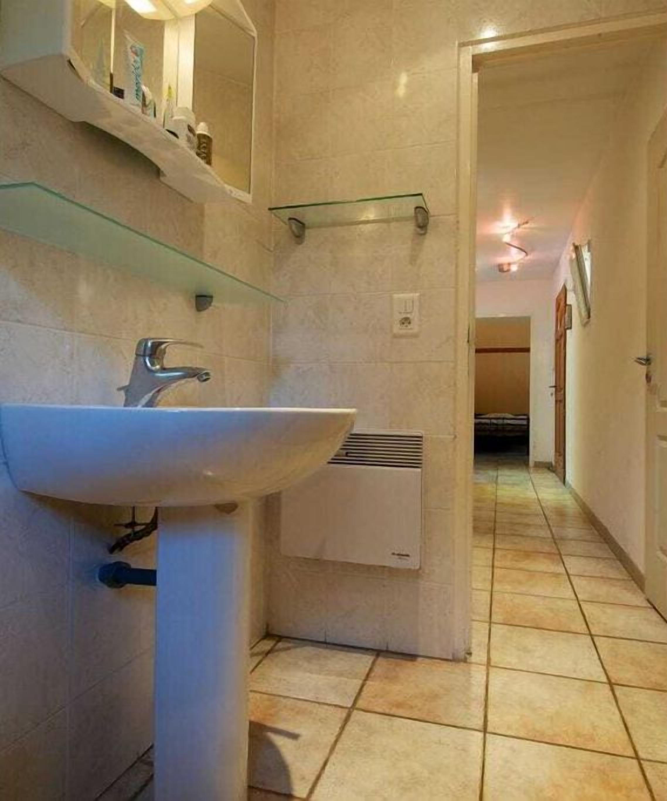 Un baño con un lavamanos blanco, un espejo, un perchero para toallas y una unidad de ventilación.