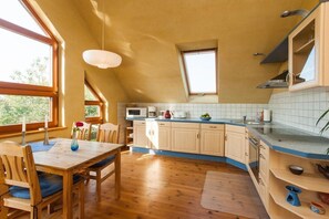 A kitchen with wooden cabinets, a dining table with chairs, and a window providing natural light. - Holiday apartment in Nieby with swimming pool (Nieby)