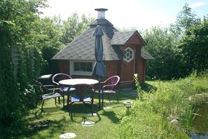 A small brick building with a chimney, a round table with chairs, and a garden area with a pond. - Holiday apartment in Nieby with swimming pool (Nieby)