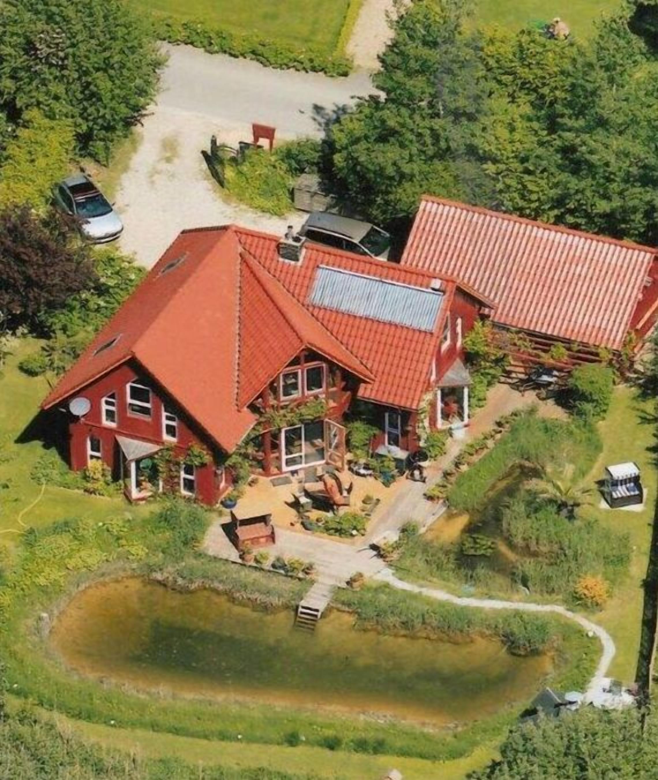 Uma casa grande com telhado vermelho, um lago e uma entrada de carros.