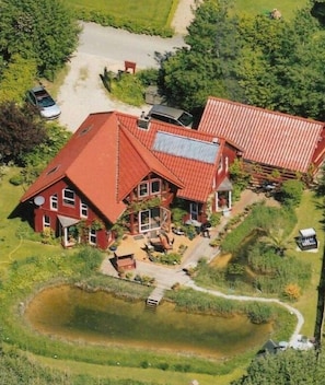 Een ruim huis met een rood dak, een vijver en een oprit.