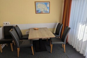 Un coin repas avec une table en bois et des chaises noires, une carte accrochée au mur et une fenêtre avec des rideaux.