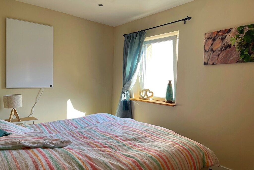 Een slaapkamer met een bed, een bedlampje, een raam met gordijnen en een aan de muur hangend schilderij.
