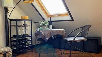 Een gezellig zolderkamertje met dakraam, een eettafel, stoelen, een wijnrek en een mand.