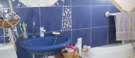 A bathroom with a blue sink, a white bathtub, and a mirror above the sink.