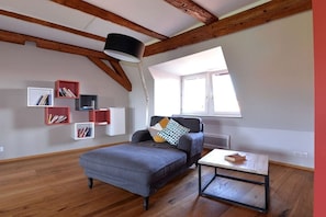 Ein Zimmer mit freiliegenden Holzbalken, einem grauen Sofa, einem kleinen Tisch und einer Einbauschränke mit Büchern.