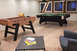 Ein Zimmer mit einem Kicker, einem Billardtisch und einem kleinen Tisch mit Büchern.