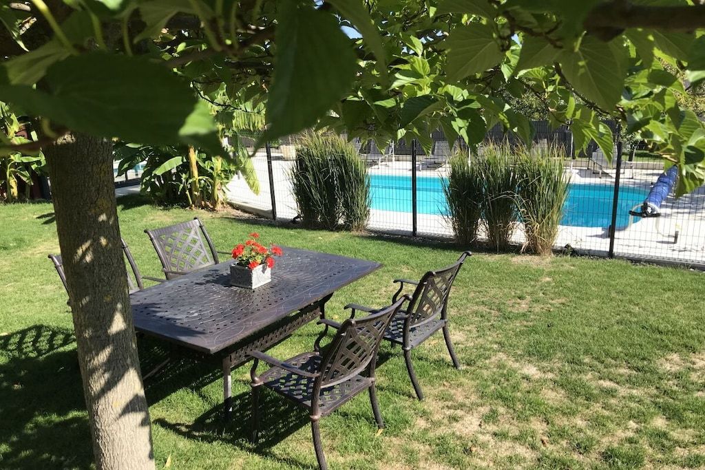 Eine Terrasse mit Tisch und Stühlen, ein Pool und ein Baum, der Schatten spendet.