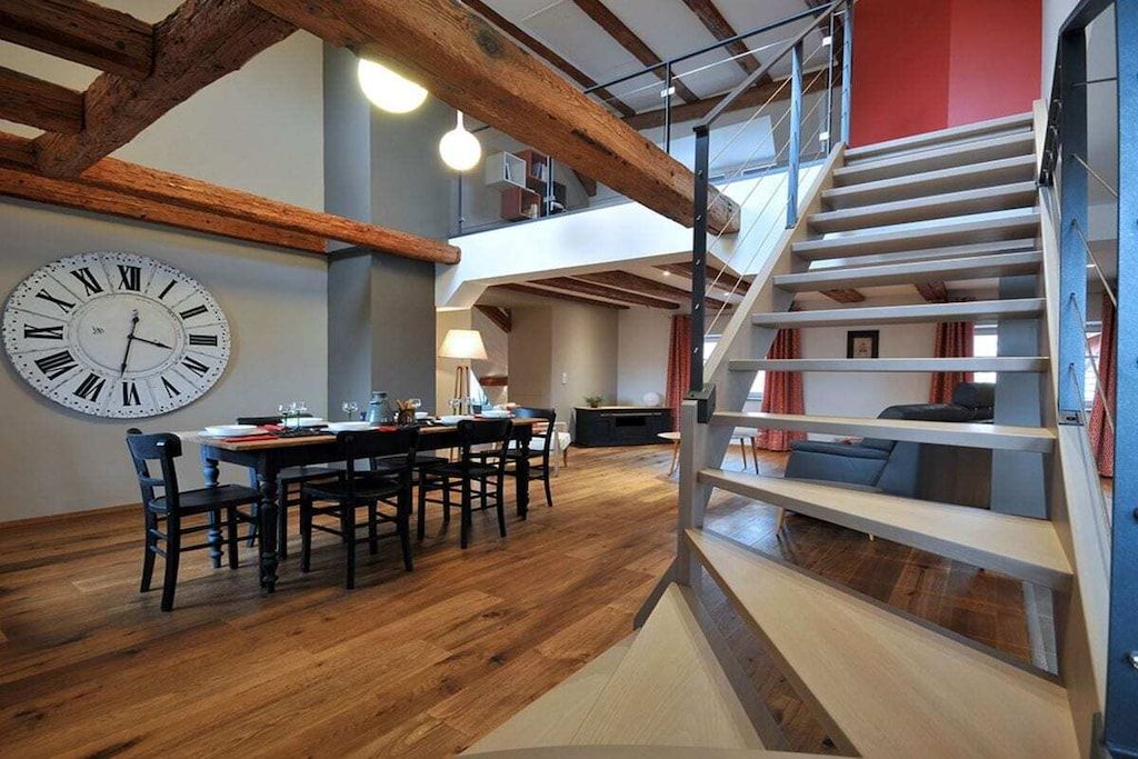 Ein Essbereich mit einer großen Wanduhr, Holzboden und einer modern gestalteten Treppe.