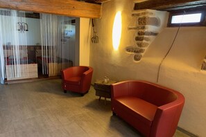 Een kamer met een houten plafond, een stenen muur met een lamp, een rode bank en een klein tafeltje.